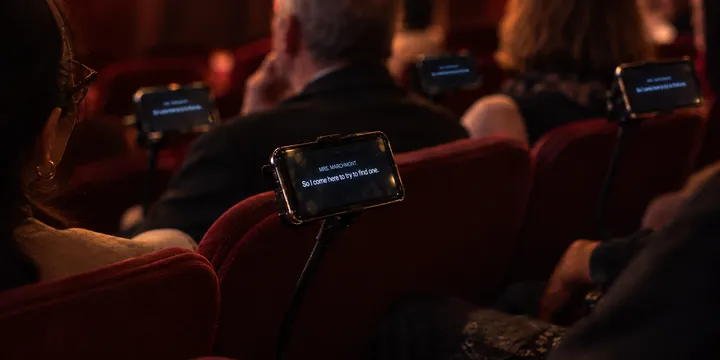 Espectadores lendo sobretítulos em celulares gerenciados durante uma apresentação teatral