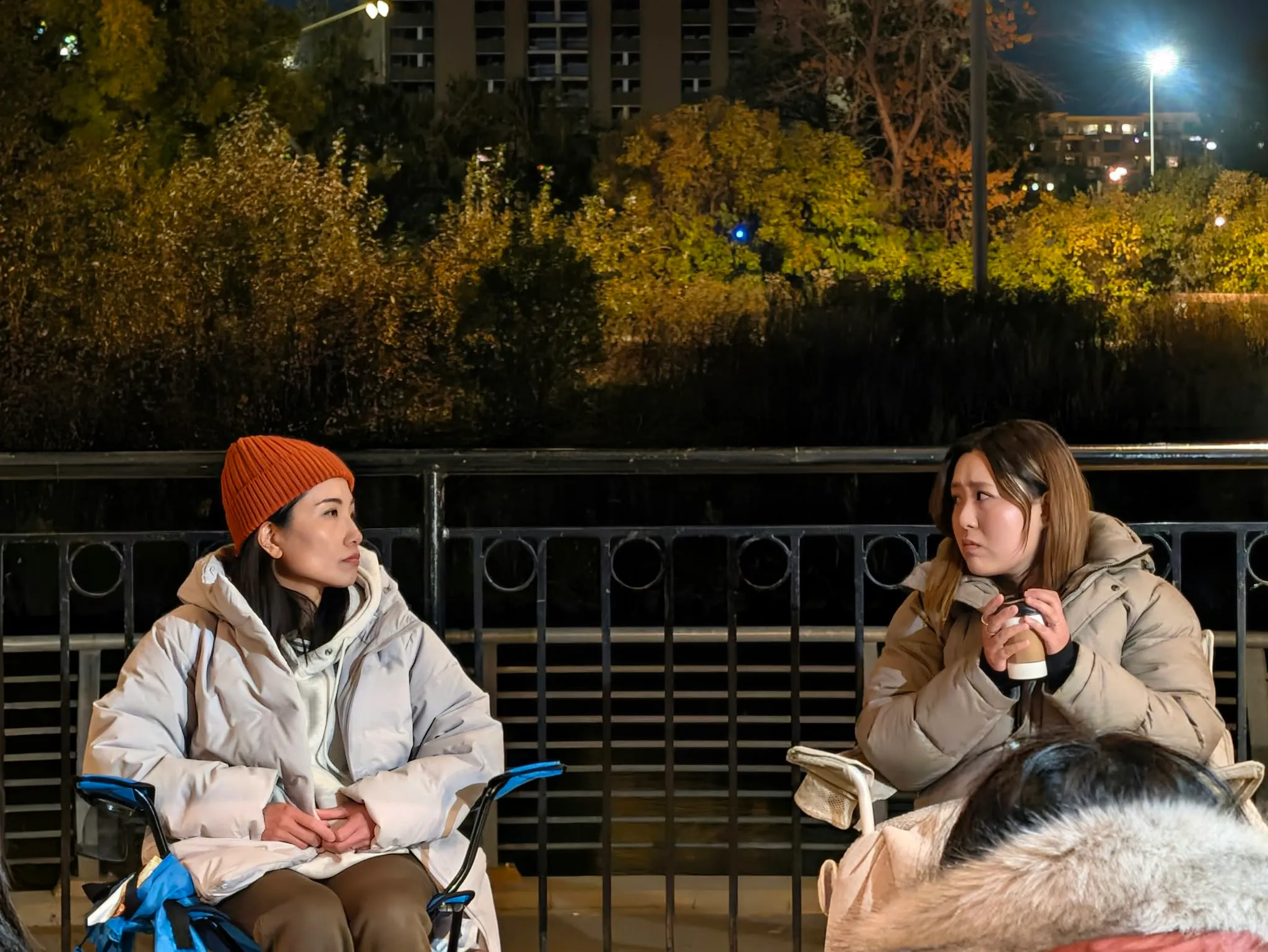 Two women sit facing one another beneath the pavilion roof at night