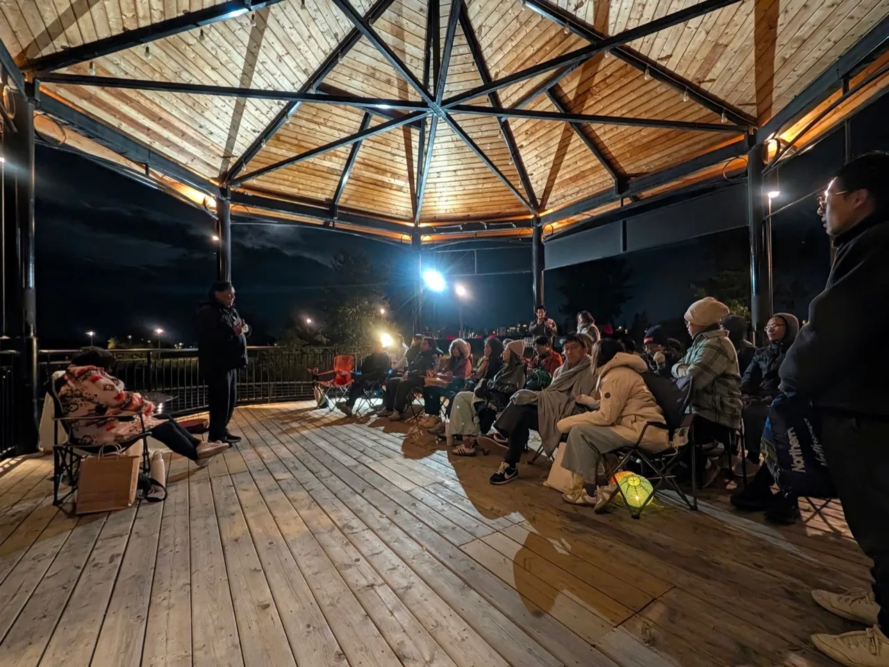 Audience members listen to a speaker in the open-sided Music Pavilion at night